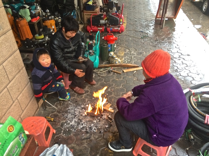 Local shop owners trying to warm up around a sidewalk fire (since it's probably colder inside!)